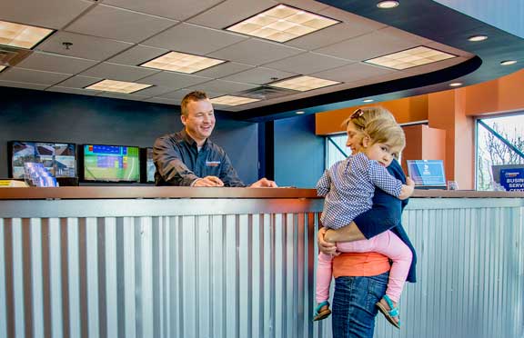 Front desk employee at Guardian Storage explains how to choose self storage units to a mom holding her little girl in her arms.