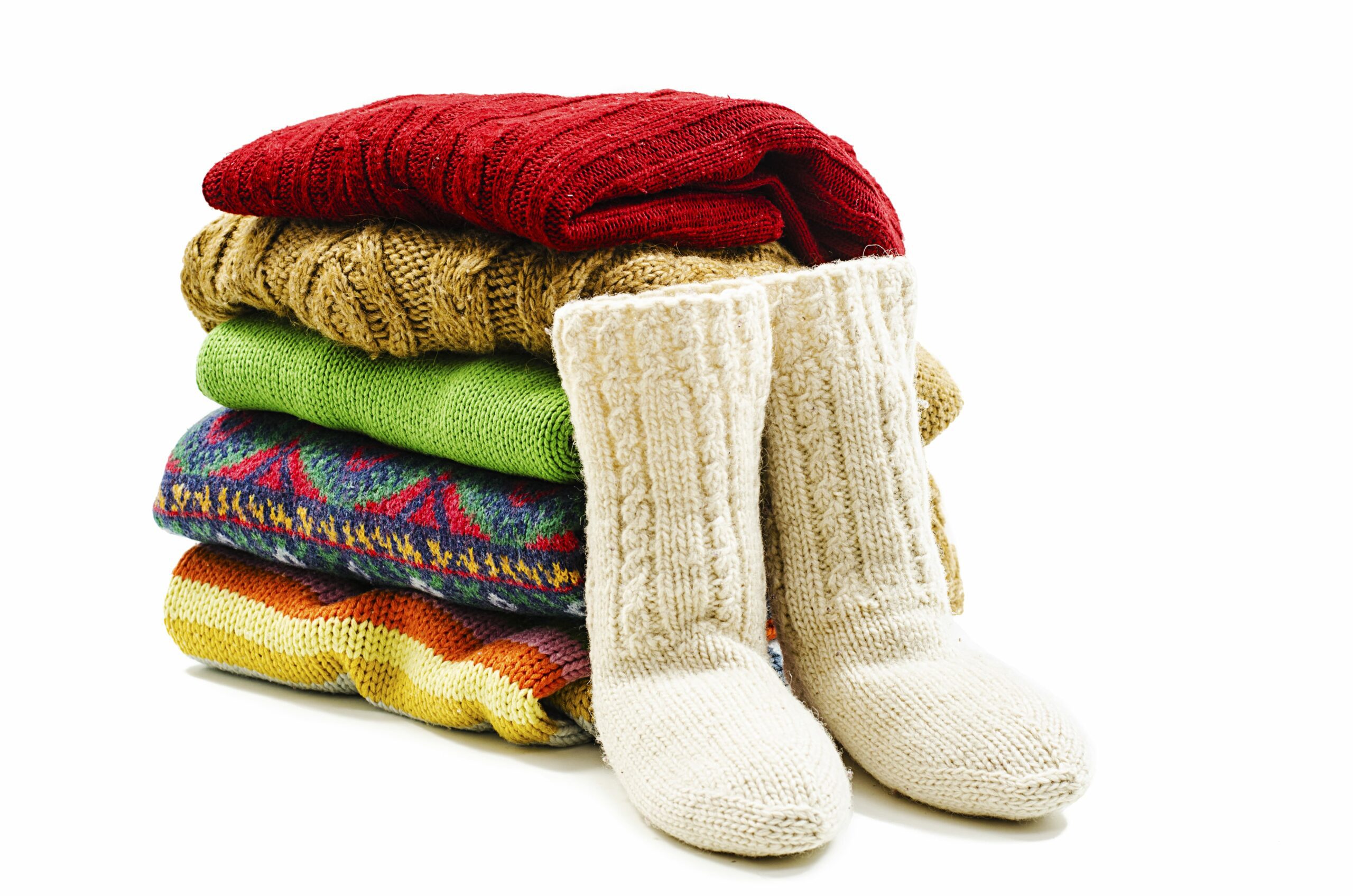 A neat pile of colorful sweaters sit next to a pair of cozy wool slippers, ready to be prepped for winter storage.