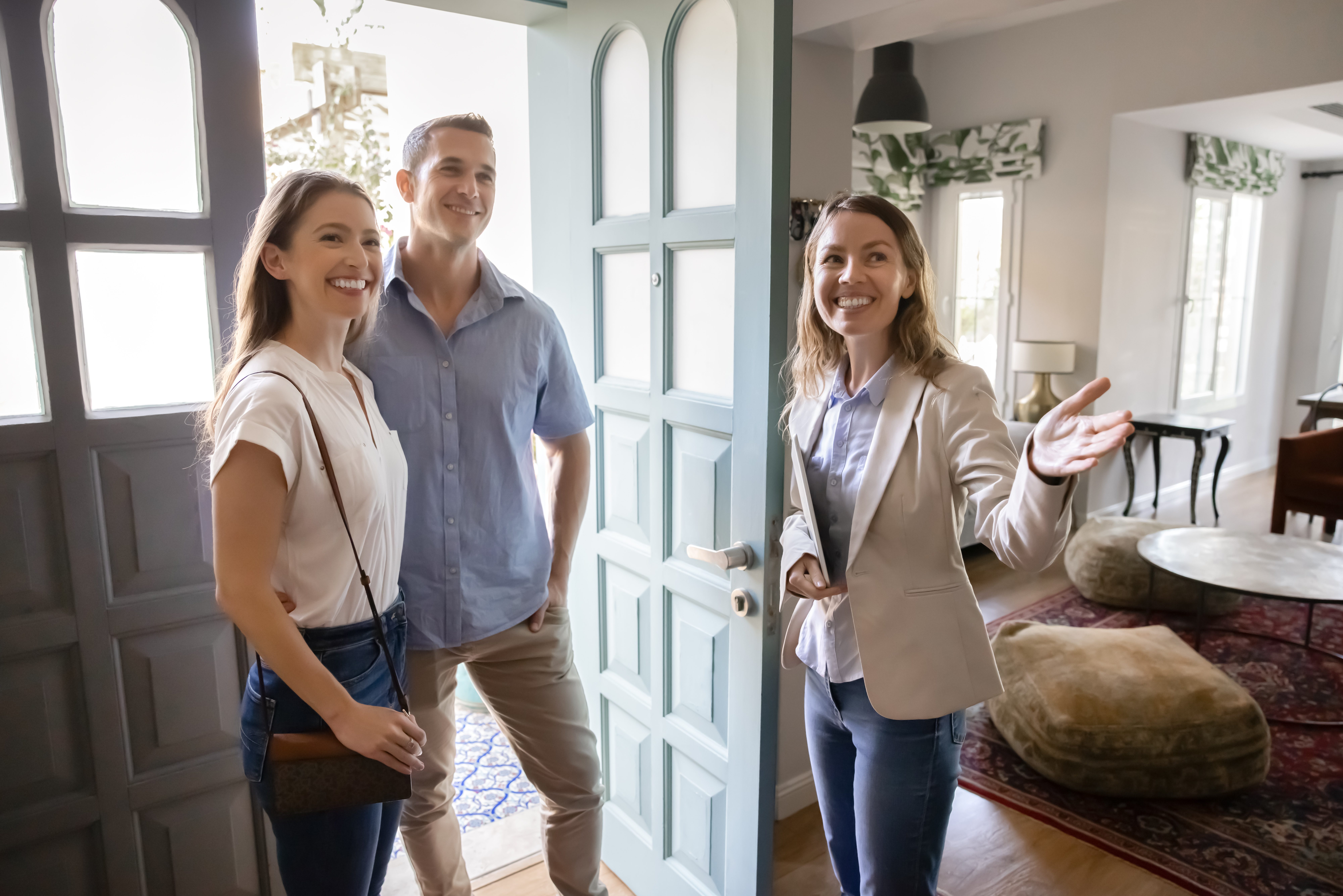 Positive, real estate agent welcoming young married couple into house for sale or renting, showcasing new property, provide professional services during formal meeting. Homeownership, consultation