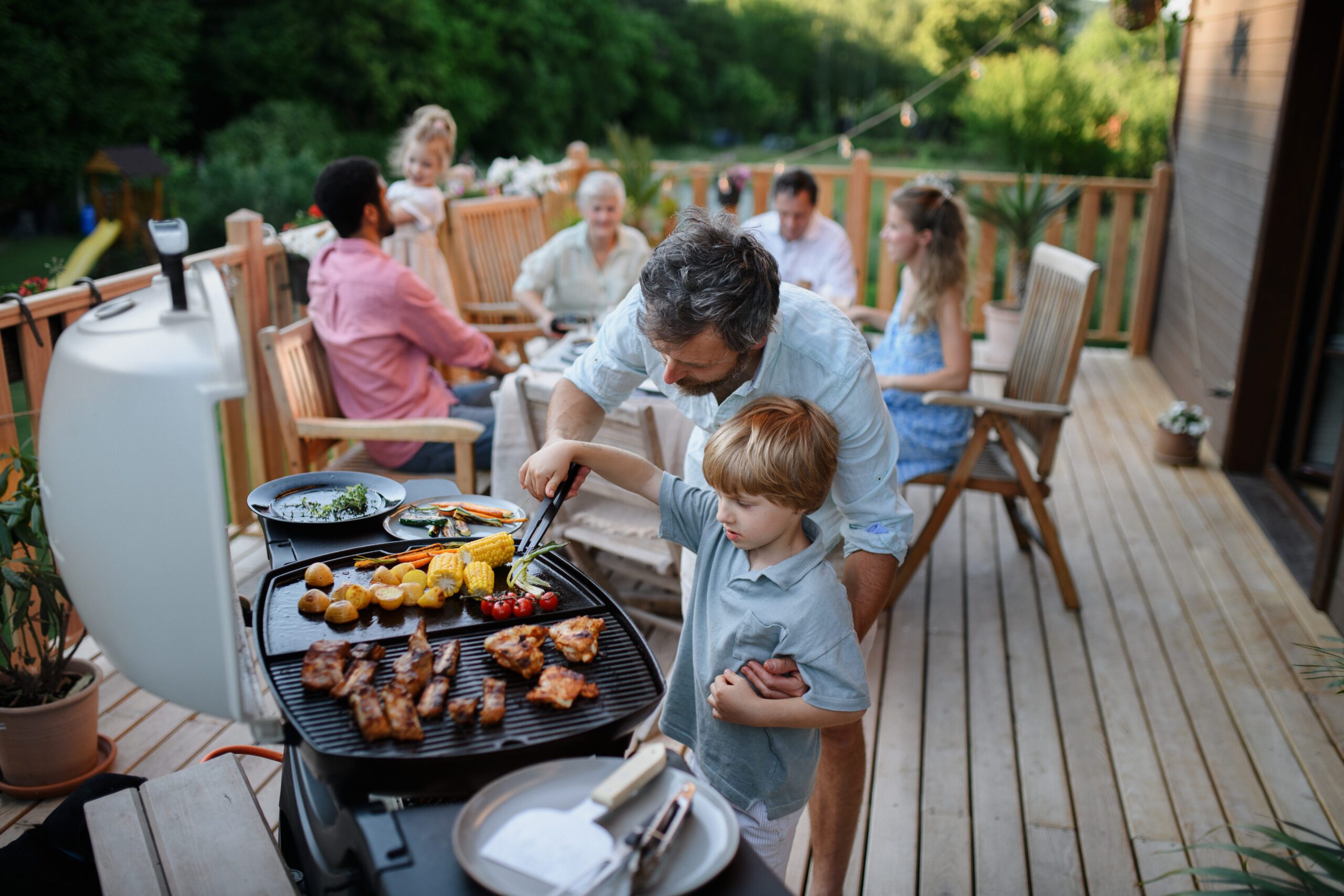 Father with son grilling outside during family summer garden party.