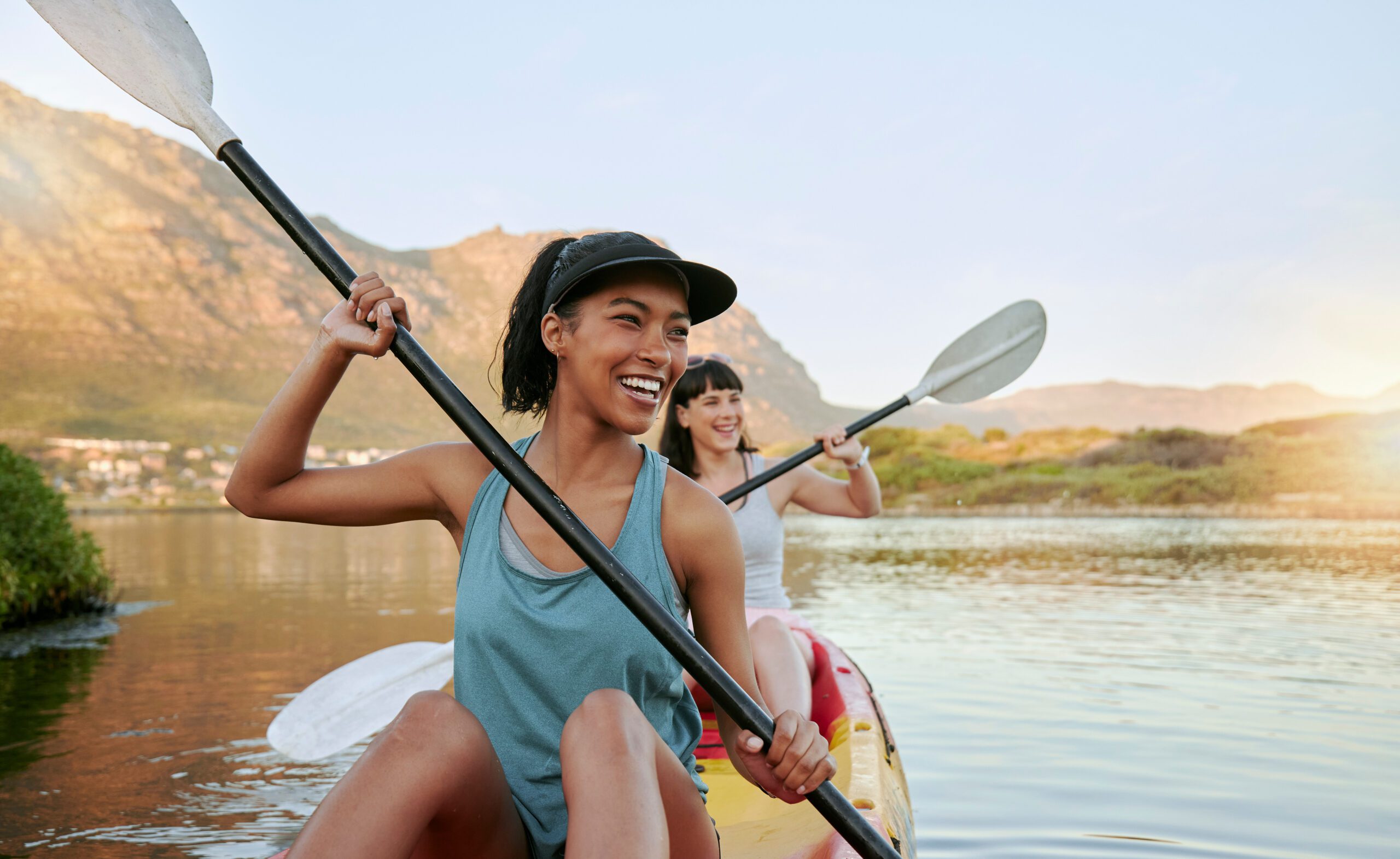 Two smiling friends kayaking on a lake together during summer break. Smiling and happy playful women bonding outside in nature with water activity. Having fun on a kayak during weekend recreation.