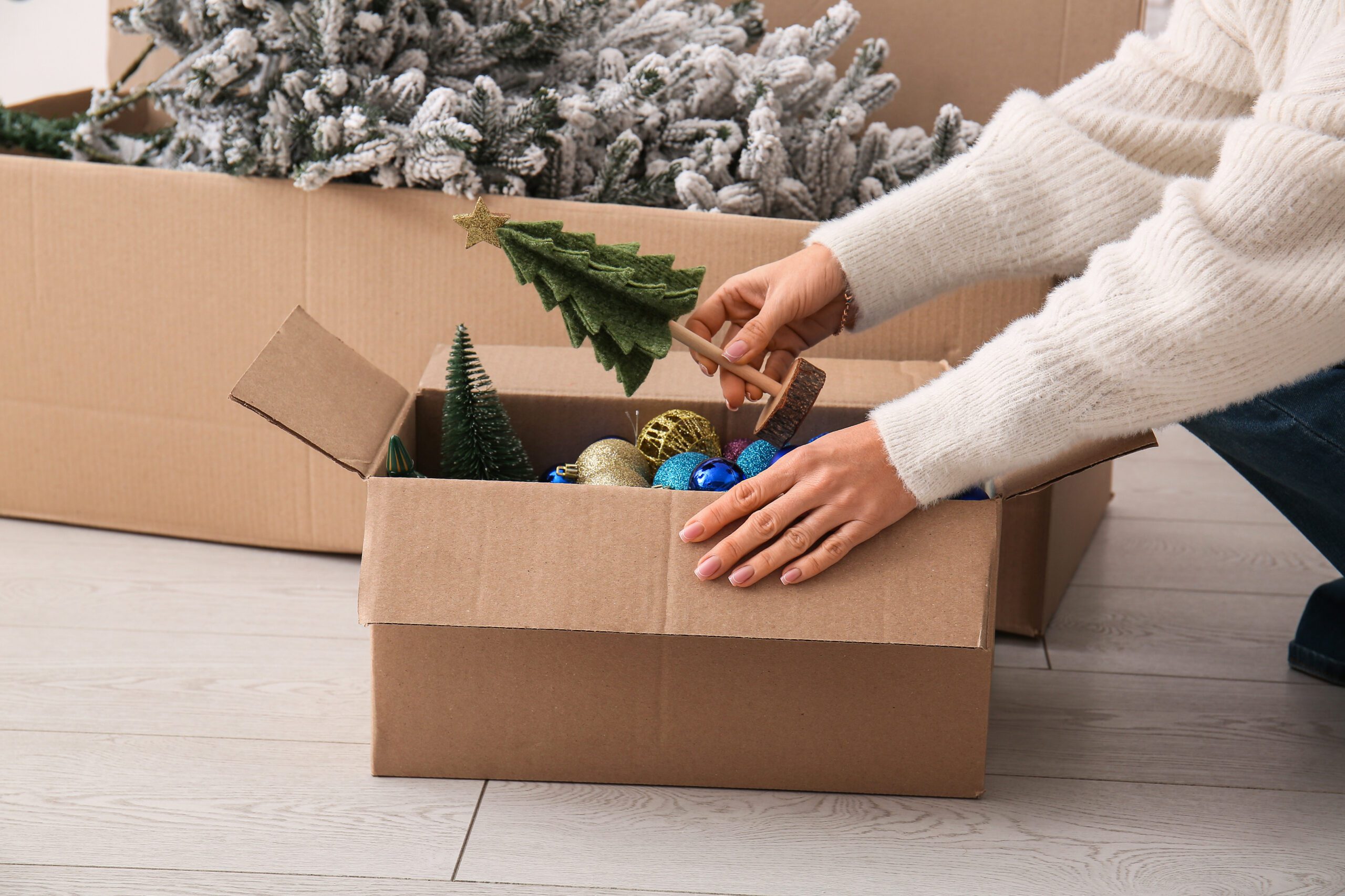 Woman putting Christmas toys in cardboard box at home, closeup
